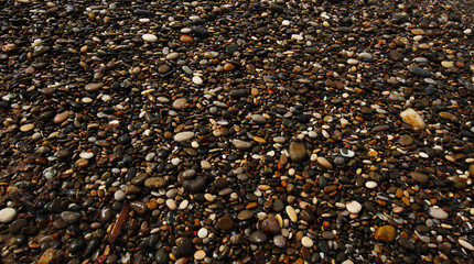 Small pebbles of different shades of gray, brown, yellow, green and blue pebbles. Mediterranean sea coast, natural background. Wet stones, sea shore
