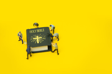 Miniature people : Worker try to fix and open Holy bible on yellow background.body of christ and church bible study group concept.