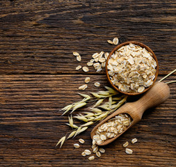 Oat flakes in Wooden bowl and spoon with oat plant on old wooden table. Top view