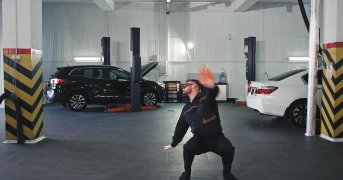 Very excited modern mechanic guy dancing it n and moving charismatic in front of the camera in a spacious and modern service auto center