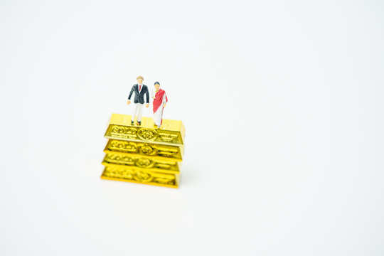 Miniature People :Senior Indian Couple And Rich People Stand On Pile Of Gold Bar On White Background.Concept For Money, Financial, Business Planning,Gold Business And Rich People In India.