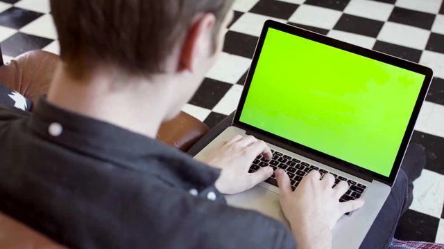 Close-up of young man typing at laptop with green scree. Stock footage. Young programmer or freelancer working at laptop with green screen