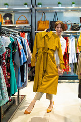 Beautiful caucasian woman try on a mustard coat and smiles in a big mall