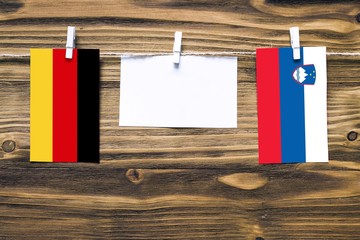 Hanging flags of Germany and Slovenia attached to rope with clothes pins with copy space on white...