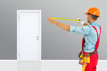 Worker in hard hat measure with ruler. Young handyman installing a white door with in a room