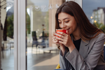 Pretty young fashion woman looking cheerful and happy chatting on social media on smart phone app while drinking coffee in urban city. In lifestyle mobile use and online app and technology concept.