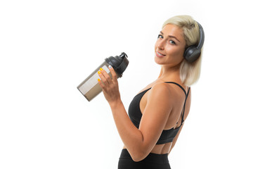 Sport caucasian blonde girl with earphones do sports, smiles and drinks water from sport bottle