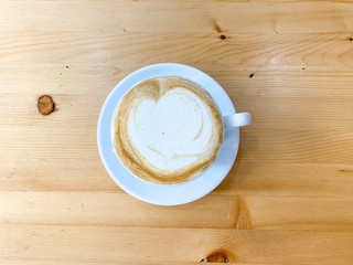 White cup of hot coffee with latte art on wooden table