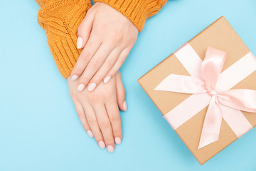 Beautiful female hands with pink manicure on nails in warm knitted sweater blue background with gift craft box baht, top view