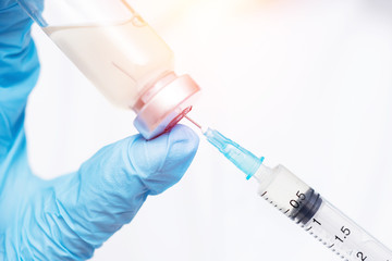 Doctor hand holding syringe and vaccine in blue gloves white coat, sun light. Concept disease injection