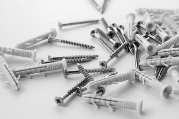 A small number of screw anchors that are scattered on a white background. Plastic plugs with screws for repair. - obrazy, fototapety, plakaty