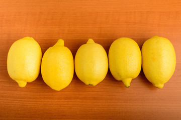 Five fresh yellow lemons an a wooden brown table, displayed in horizontal line,  top view or flat lay photo of healthy fruits