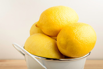 Four fresh yellow lemons in a white bowl on a wooden brown table, side view photo of healthy fruits