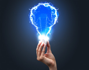 Hand holding shiny light bulb on dark background. New idea concept