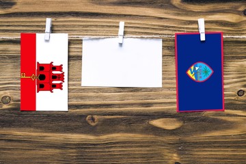 Hanging flags of Gibraltar and Guam attached to rope with clothes pins with copy space on white note paper on wooden background.Diplomatic relations between countries.