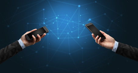Close up of two hands holding smartphones to each other, wireless connection concept