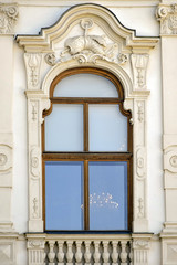 Fototapeta na wymiar Palace window with exquisite stucco ornament. Rich decoration of old historical building in Belvedere Palace. Vienna, Austria. Front view. The lights of lit chandelier are visible in window.