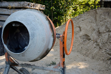 Electric concrete mixer on the background of a heap of sand. Construction machinery at the...