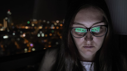 Fototapeta na wymiar Portrait of young brunette woman in glasses working on computer near the window with cityscape view, copy space.Overtime work at night, young careerist.