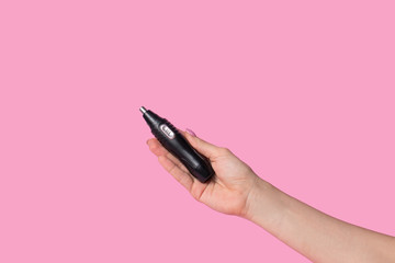 Female hands gently hold a male black electric trimmer. Minimalism on a pastel pink background.