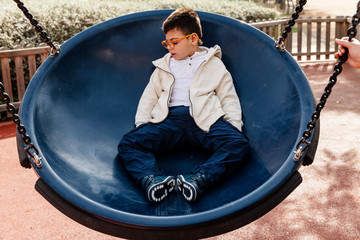 niño en el parque en columpio grande redondo balanceándose y riendo . Niño con pluri...