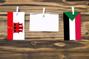 Hanging flags of Gibraltar and Sudan attached to rope with clothes pins with copy space on white note paper on wooden background.Diplomatic relations between countries.