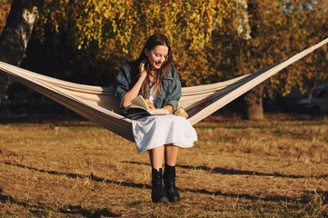 Young woman reading book in comfortable hammock in the park.