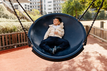 niño en el parque en columpio grande redondo balanceándose y riendo . Niño con pluri...