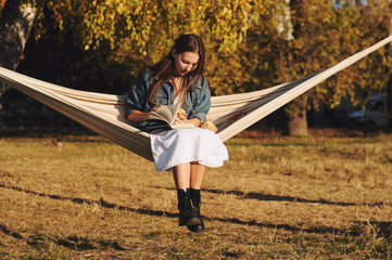 Young woman reading book in comfortable hammock in the park.