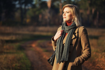 Young fashion blonde woman in beige coat and gray scarf walking outdoor