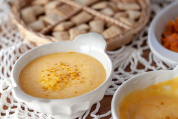 Pumpkin cream spiced with curry in a white bowl and some roasted pumpkin dice and croutons. Close Up