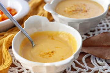 Pumpkin cream spiced with curry in a white bowl with a spoon and some roasted pumpkin dice and croutons. Close Up