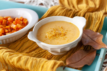 Pumpkin cream spiced with curry in a white bowl with roasted pumpkin and bread. Close Up