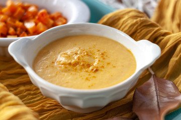 Pumpkin cream spiced with curry in a white bowl with roasted pumpkin and bread. Close Up