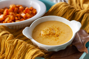 Pumpkin cream spiced with curry in a white bowl with roasted pumpkin and bread. Close Up