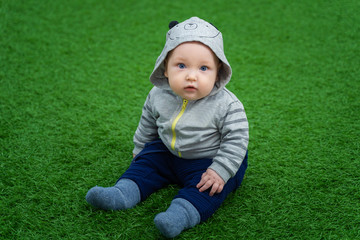 Little beautiful child sits on a green lawn and looks in surprise at the camera.