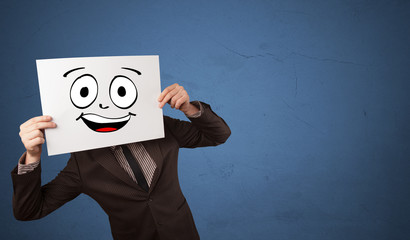 Young student holding a paper with laughing emoticon in front of his face