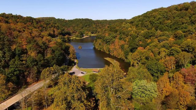 A slow forward aerial establishing shot of Bradys Run Lake in Western Pennsylvania on a sunny Autumn day.  	