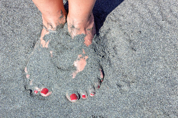 female legs with red pedicure on a background of black sand