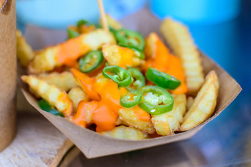 French potato fried with cheese cream and  chopped jalapenos peppers, displayed for sale at a street food market in direct sunlight, selective focus