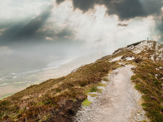 Diamond hill, Connemara National park, county Galway, Path to the top, silhouette of a hiker on the peak, dramatic cloudy sky. Concept travel, hiking, tourism.