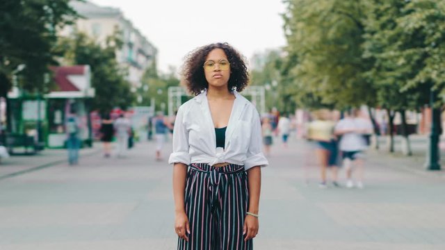 Time lapse of pretty Afro-American student serious girl standing in urban street outdoors looking at camera. Individuality, character and casual life concept.