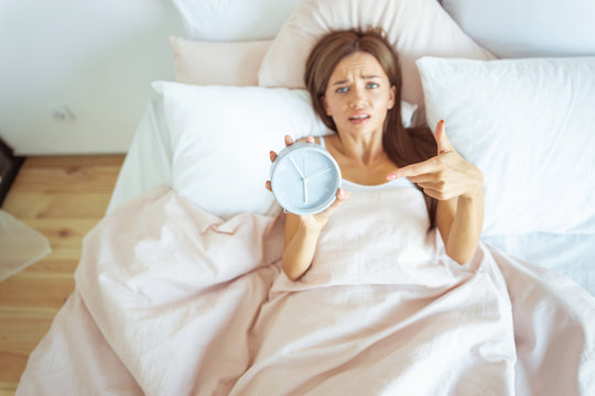 Young female person pointing at her alarm-clock