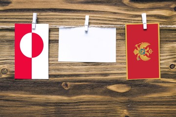 Hanging flags of Greenland and Montenegro attached to rope with clothes pins with copy space on white note paper on wooden background.Diplomatic relations between countries.