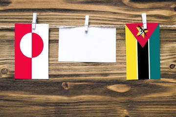 Hanging flags of Greenland and Mozambique attached to rope with clothes pins with copy space on...