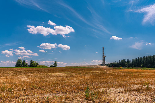 Fracking-Anlage vor Stoppelfeld unter wei&szlig;-blauem Himmel
