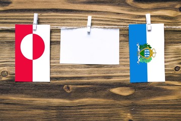 Hanging flags of Greenland and San Marino attached to rope with clothes pins with copy space on...