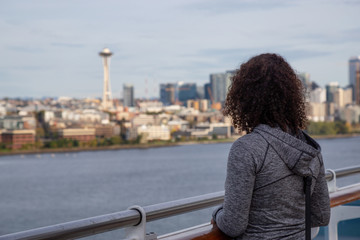 Fototapeta premium Downtown Seattle, Washington, United States of America. Girl on a Cruise Ship is enjoying the View of the Modern City on the Pacific Ocean Coast during a sunny and cloudy Autumn evening.