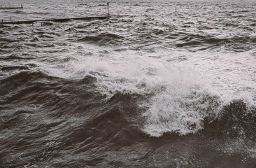 Fototapeta na wymiar Wave breaking early on a stormy day at high tide on Ramsgate West Cliff beach in black and white.