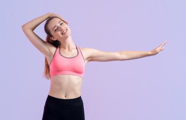 Fototapeta na wymiar Young fitness woman doing a warm-up for neck standing on a pink purple background.